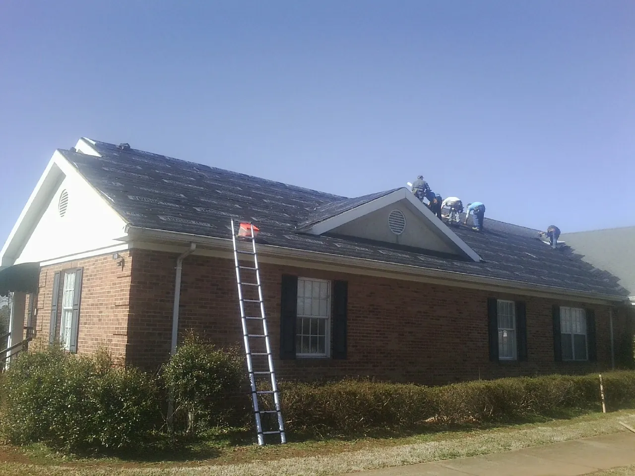 Crew tearing shingles off a brick ranch roof with a ladder set — Emergency Roof Repair work by our crew in Etna