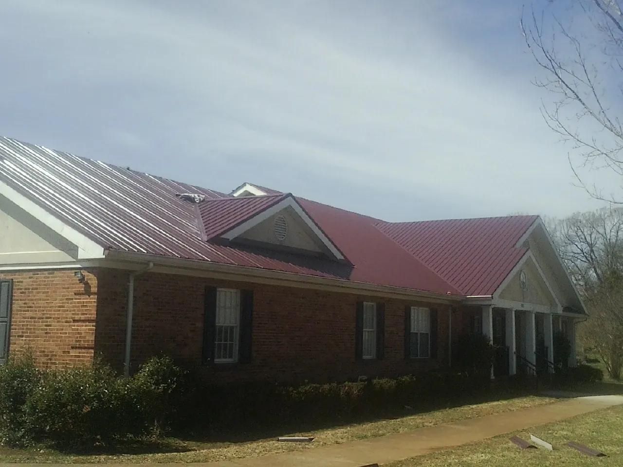 Red metal roof with gabled entries on a long brick building, from a Hail Damage Roof Repair job in Etna