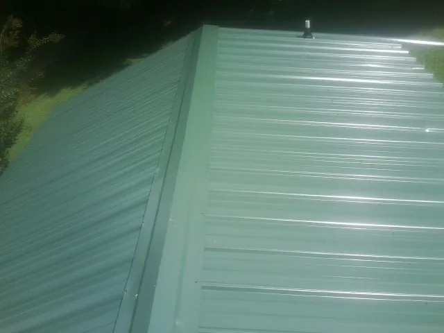 New green metal panels meeting at the ridge of a roof — Flat Roof Repair work by our crew in Etna